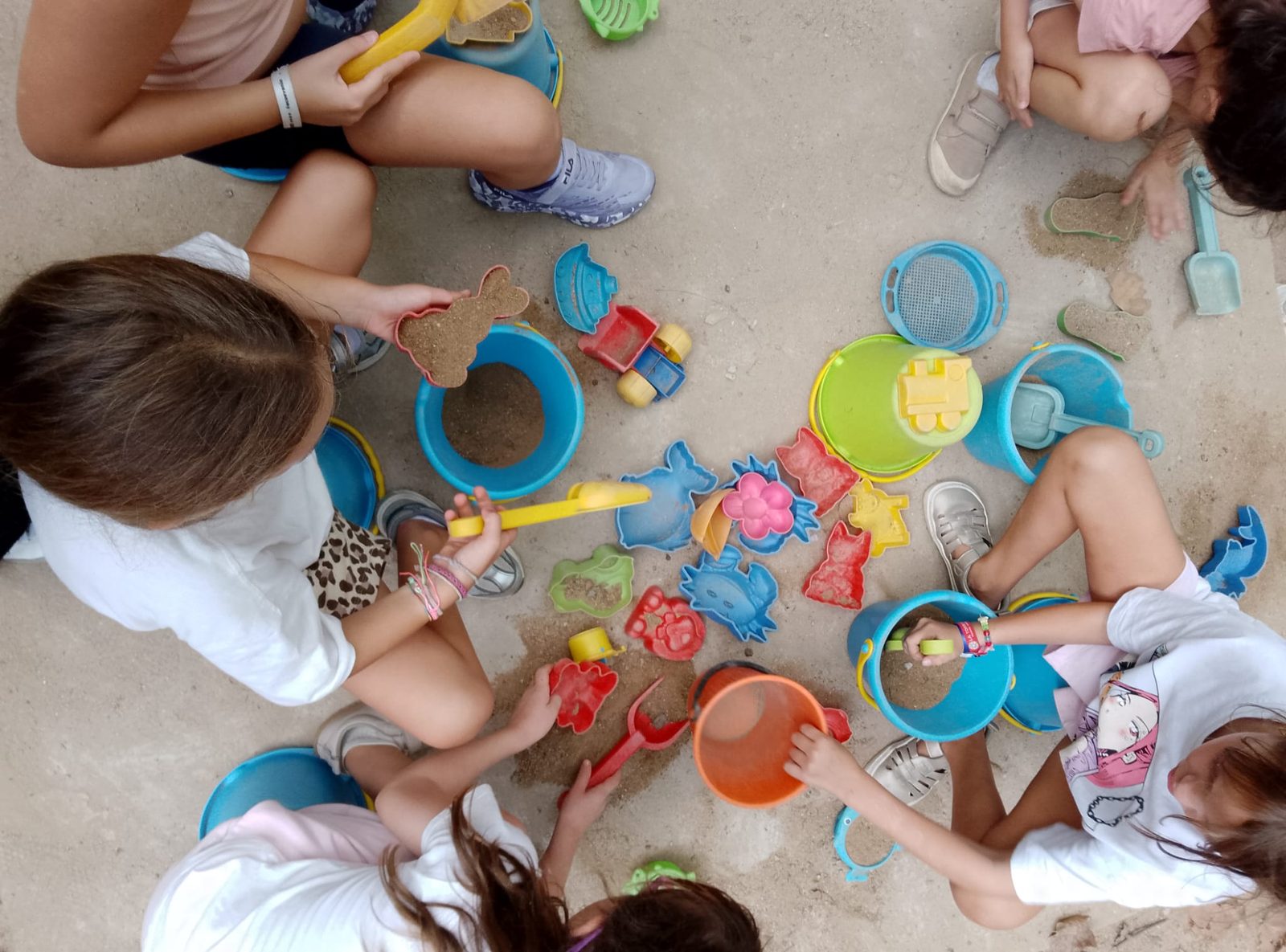 Un grup d’infants omple motlles i galledes de colors al sorral del pati.