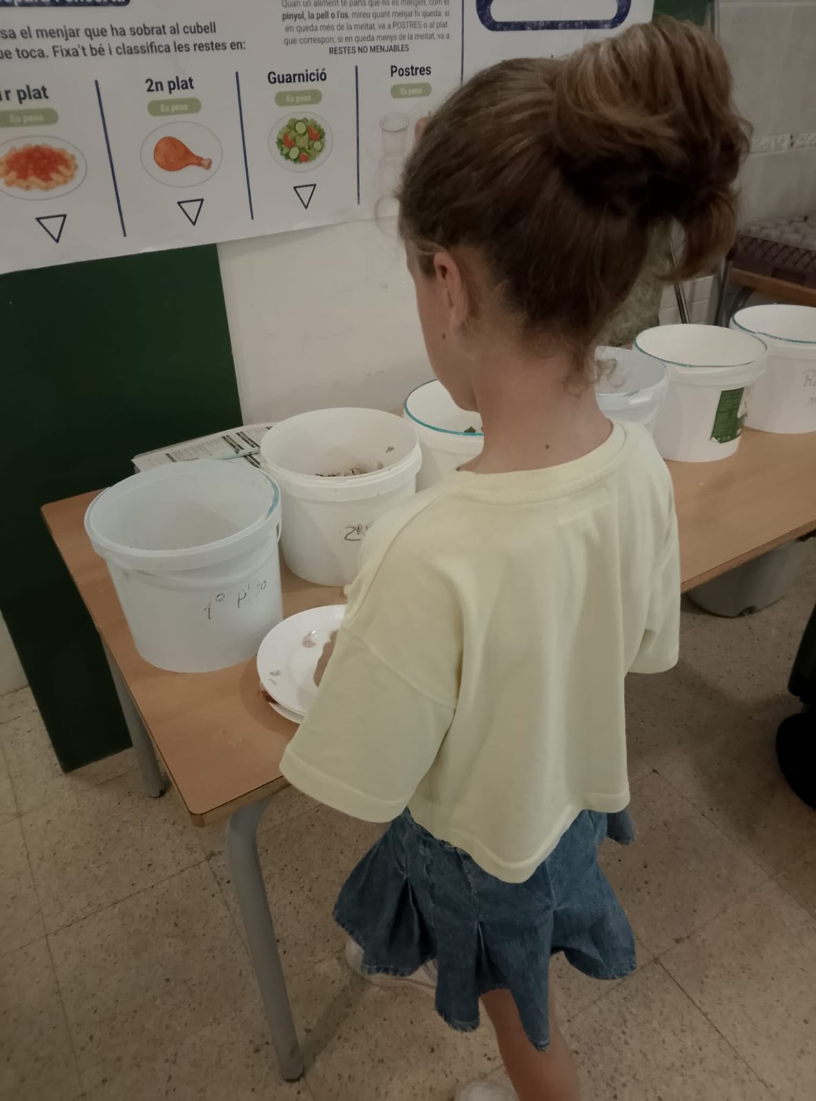 Una nena deixa el seu plat davant dels cubells senyalitzats per a cada part del menú.