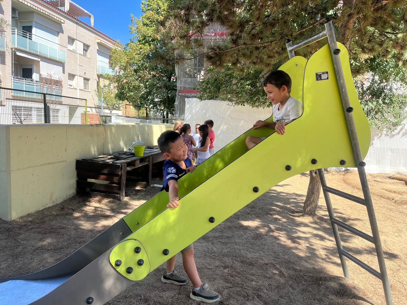 Infants pugen i baixen pel tobogan verd del pati de sorra.