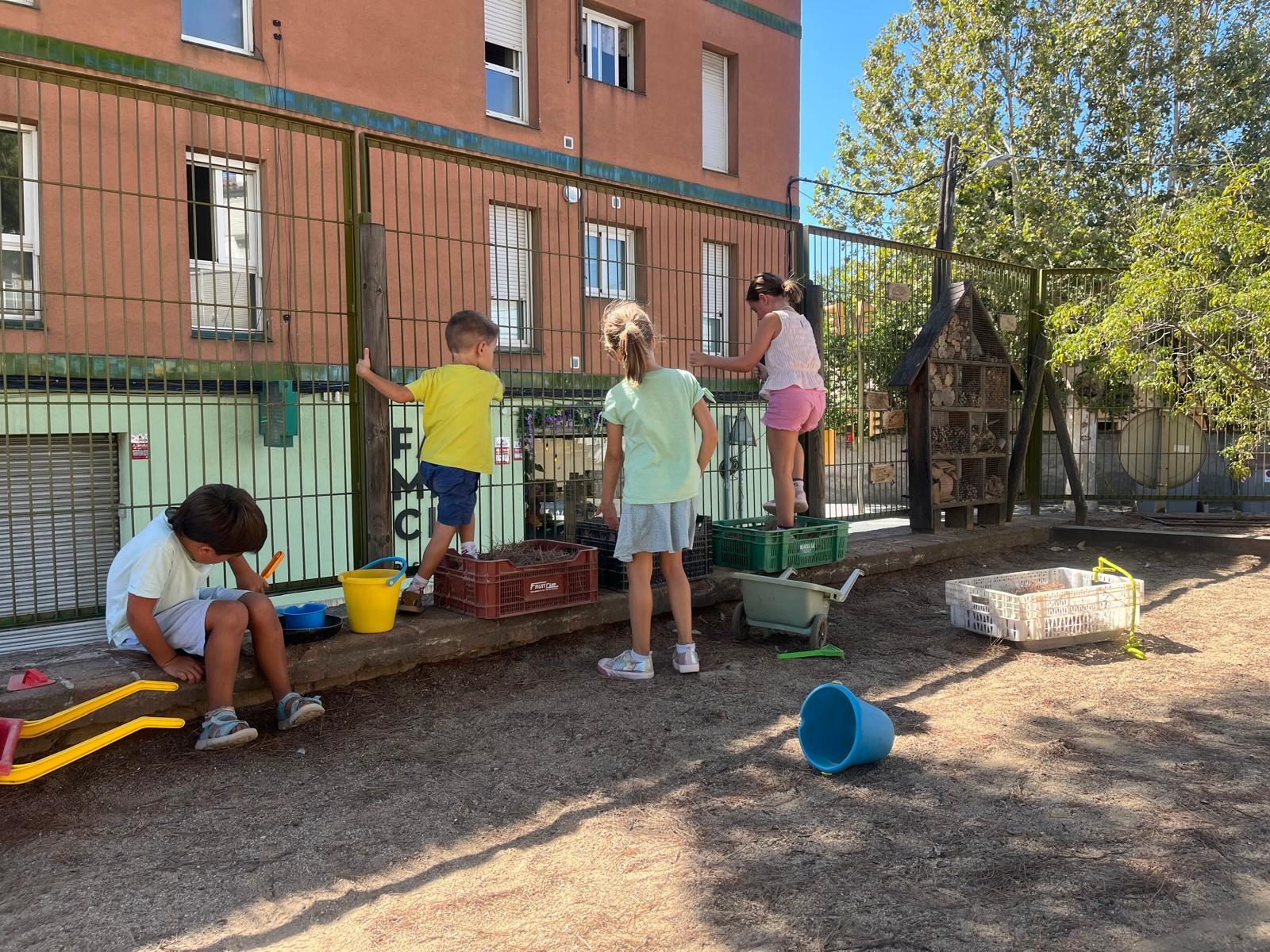 Infants amb galledes i caixes en un racó del pati, al costat de la tanca.