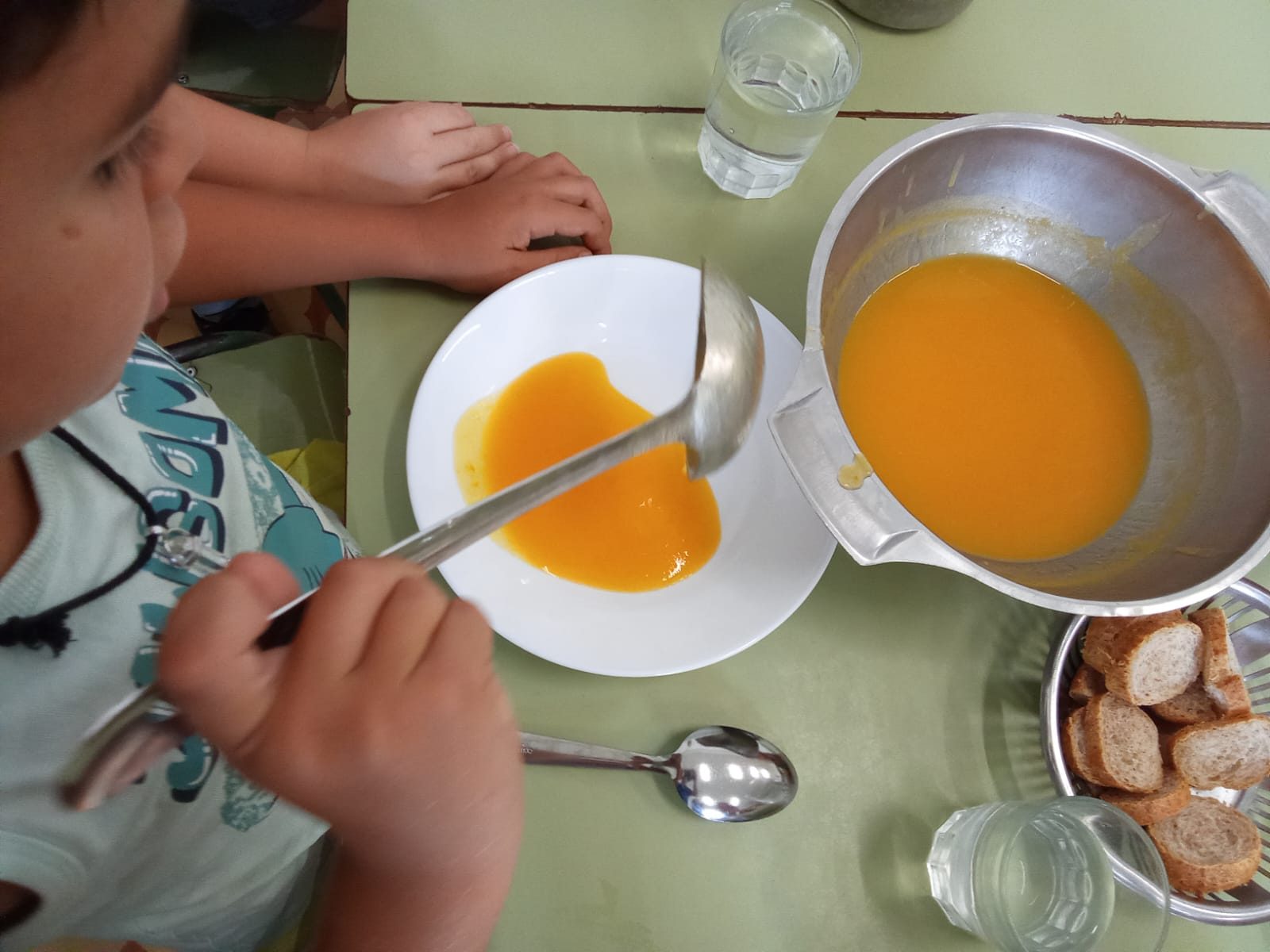 Un infant es serveix una crema amb el cullerot d’una olla col·locada al mig de la taula.