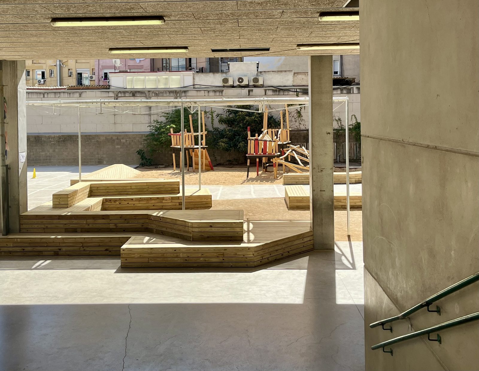 Vista del nou pati amb estructura de fusta i sorra des d’un porxo de formigó de l’escola.
