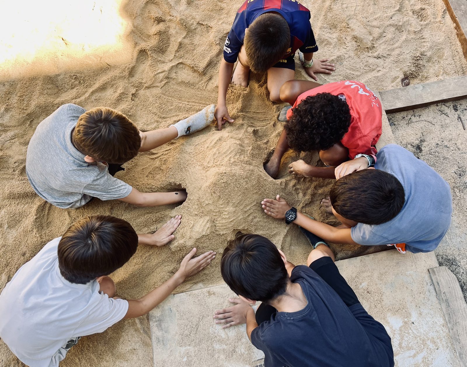 Diversos infants amb les mans dins la sorra, aplanant i excavant junts.