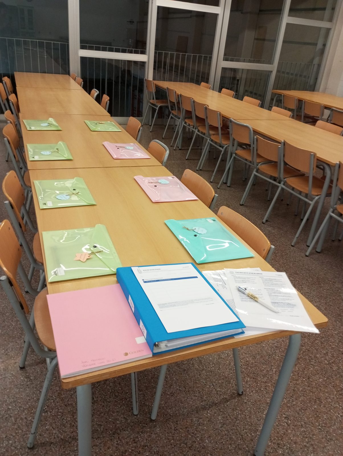 Taula llarga preparada per a una reunió, amb carpetes de colors, documentació i un dossier obert.