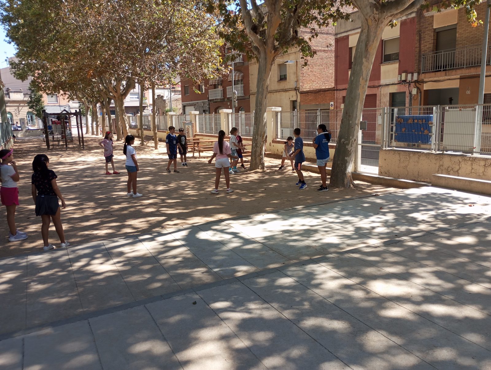 Infants jugant al pati amb taules de pícnic sota els plàtans.