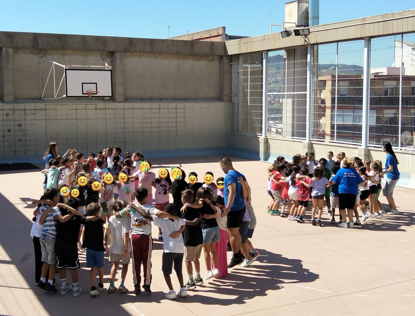 Infants i educadors formen un cercle tancat amb els braços per sobre les espatlles al mig de la pista.
