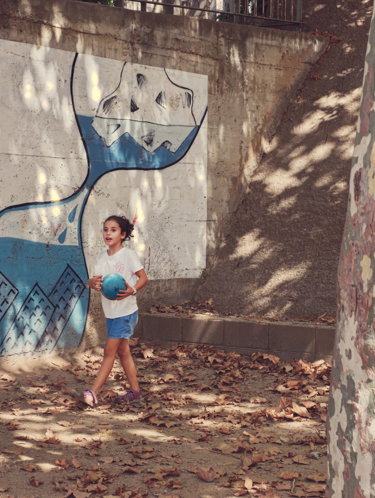 Una nena amb una pilota davant del mural blau del rellotge de sorra.