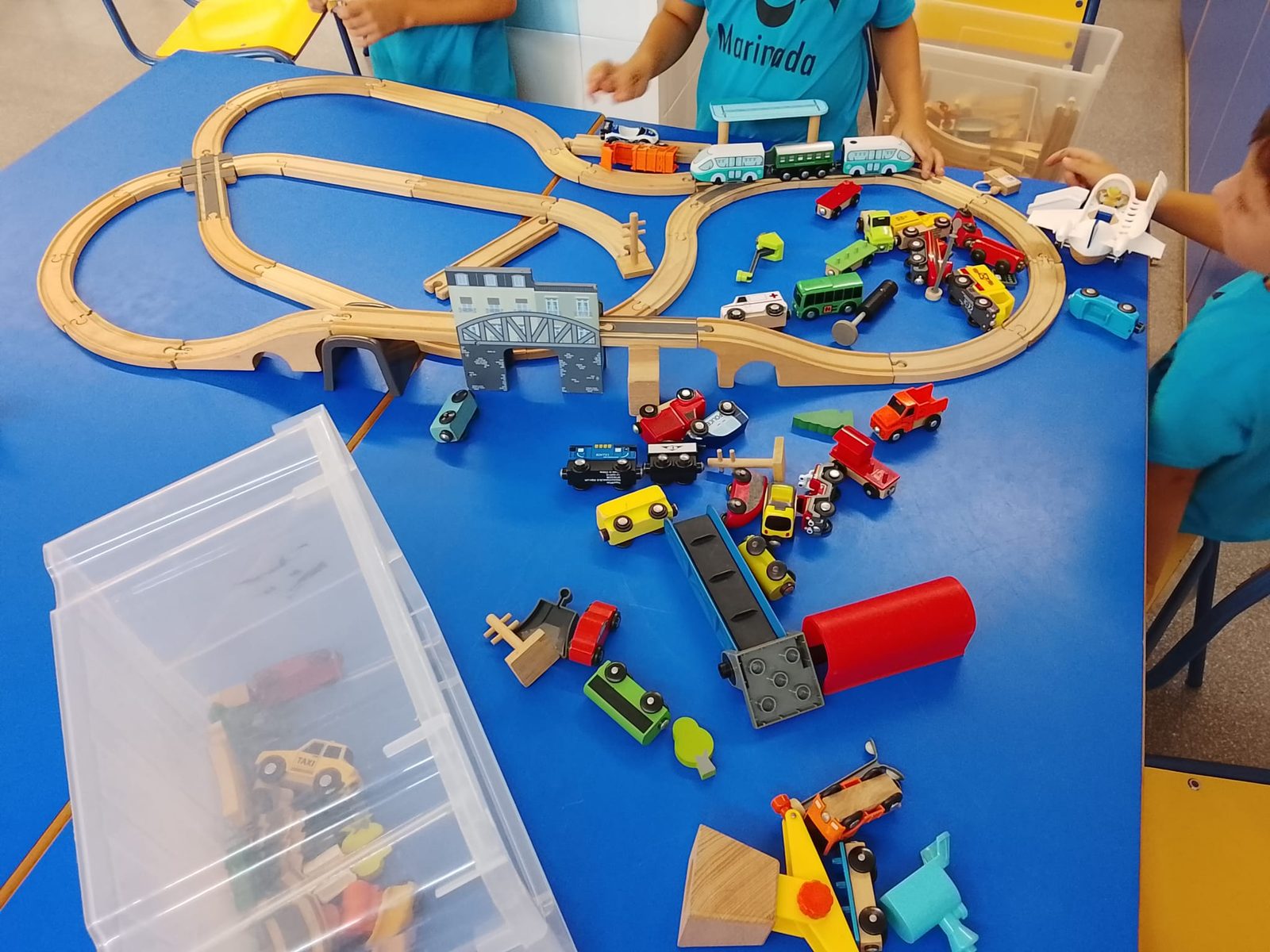 Circuit de tren de fusta muntat sobre una taula, amb vehicles i caixes de peces.