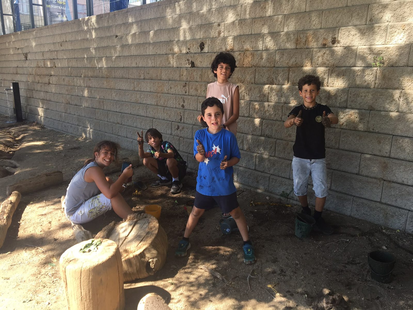 Infants al costat del sorral, amb troncs de fusta que fan de seient.