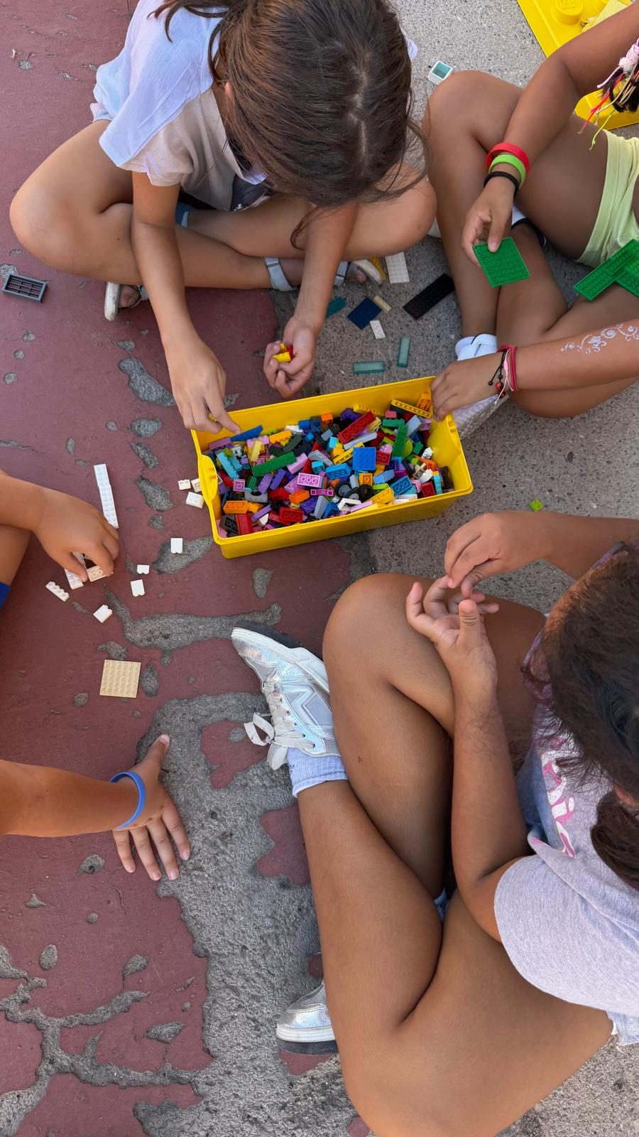 Un grup d’infants seu a terra i tria peces de construcció d’una caixa groga.